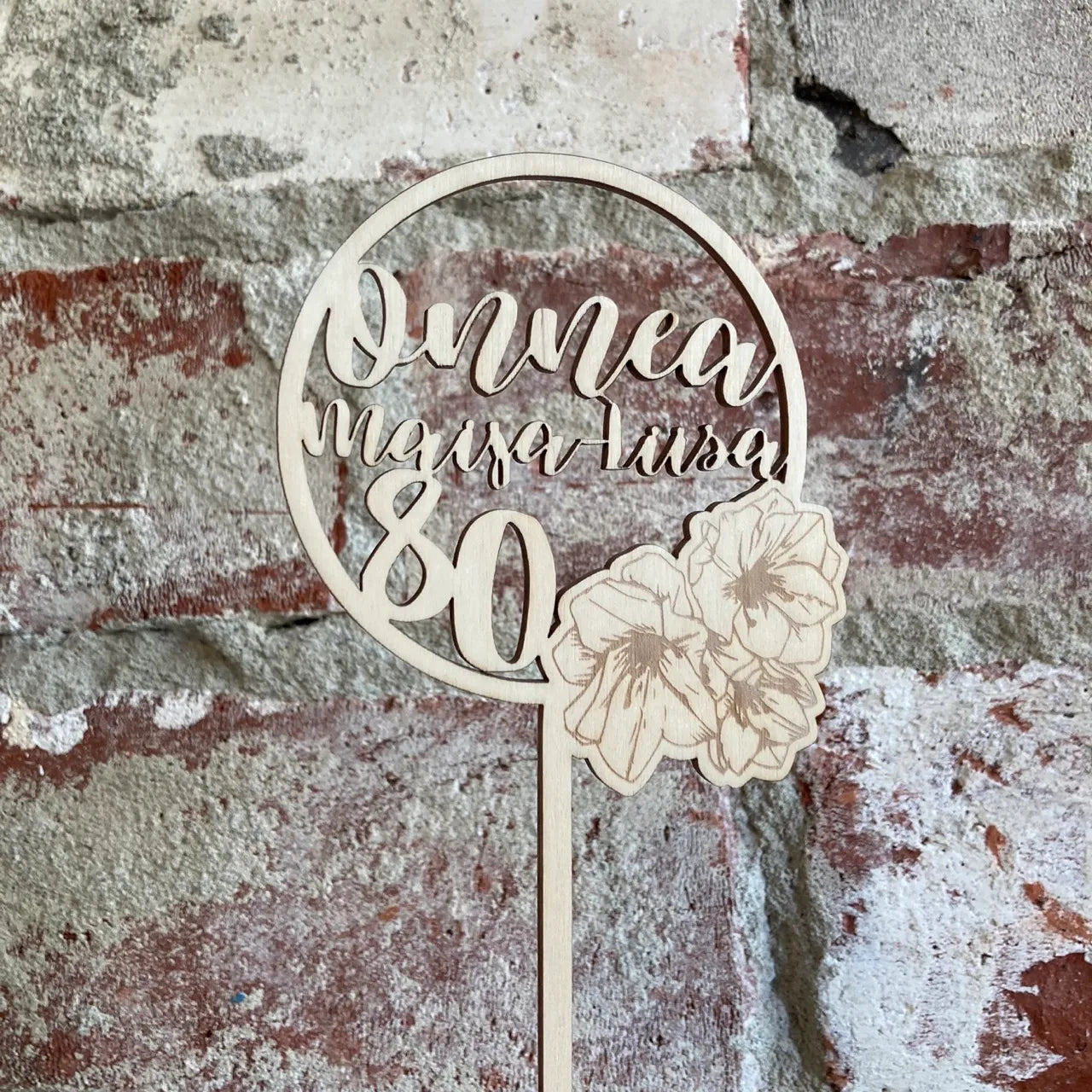 Pyöreä kakkukoriste kukka syntymäpäiväkakkuun, jossa nimi ja ikä.