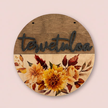 Puinen tervetuloa-kyltti syksyisellä kukkaviolla oveen.